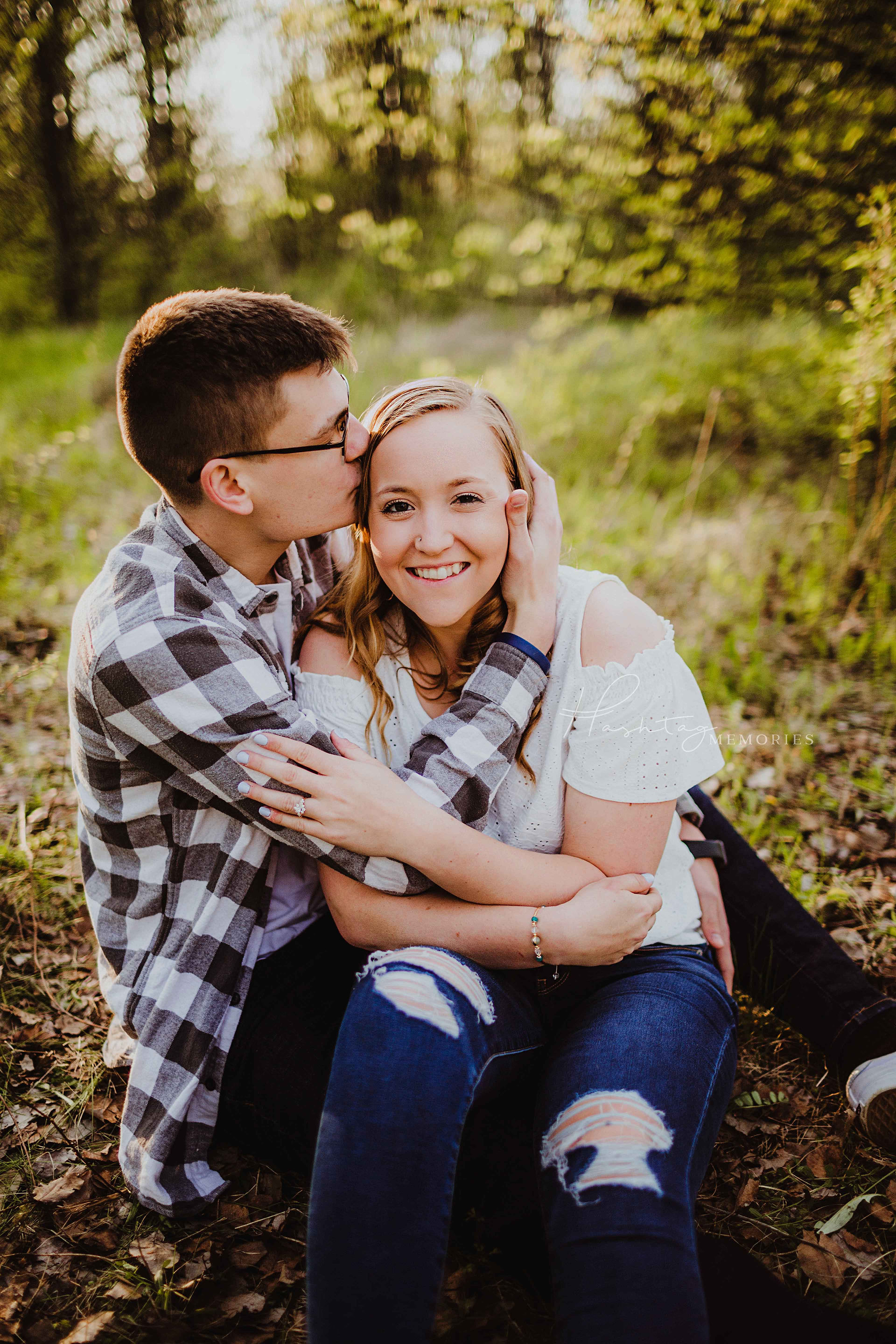 couple sits in field wrapped up together for engagement photos, in boho urban jungle setting