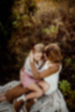 Mother and daughter embracing on a blanket in a field, surrounded by tall grass and autumn colors. Cozy and warm atmosphere.