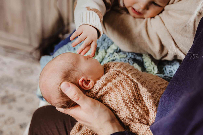 toddler big brother reaches for his new baby brother in mom and dad's arms