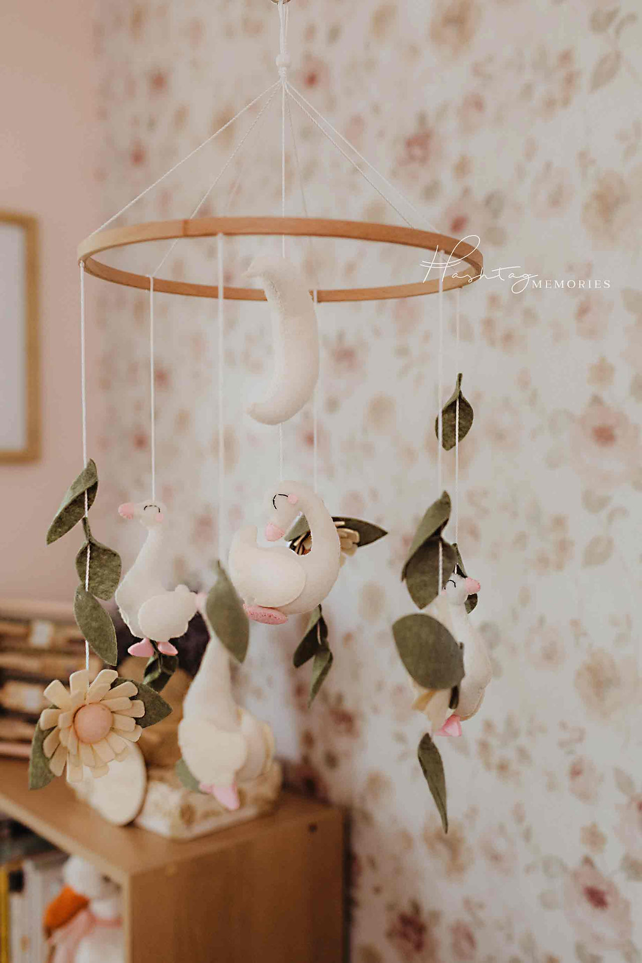 beautiful felt goose baby mobile hangs in front of pink floral wall paper in baby's nursery