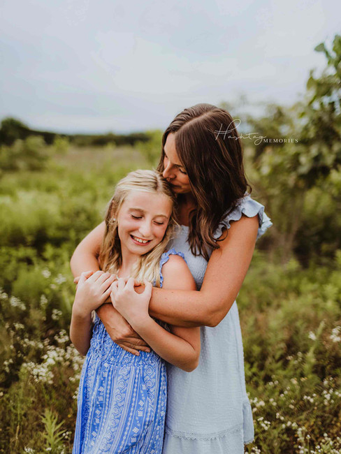 mother in blue dress wraps her arms around a tween blond daughter in a wildflower field in cicero
