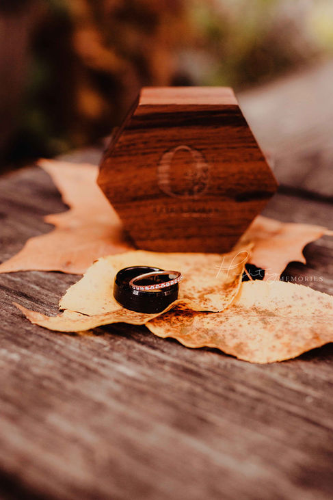 His and her wedding rings laying on top of a barrel and fall leaves for fall wedding detail photo of zionsville wedding
