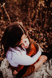 mom snuggles daughter in fall fields during family photo session