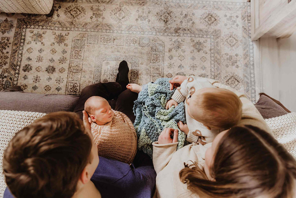 Sleeping newborn cradled in an adult’s arms, framed by blurred family members and a dog; Hashtag Memories watermark.