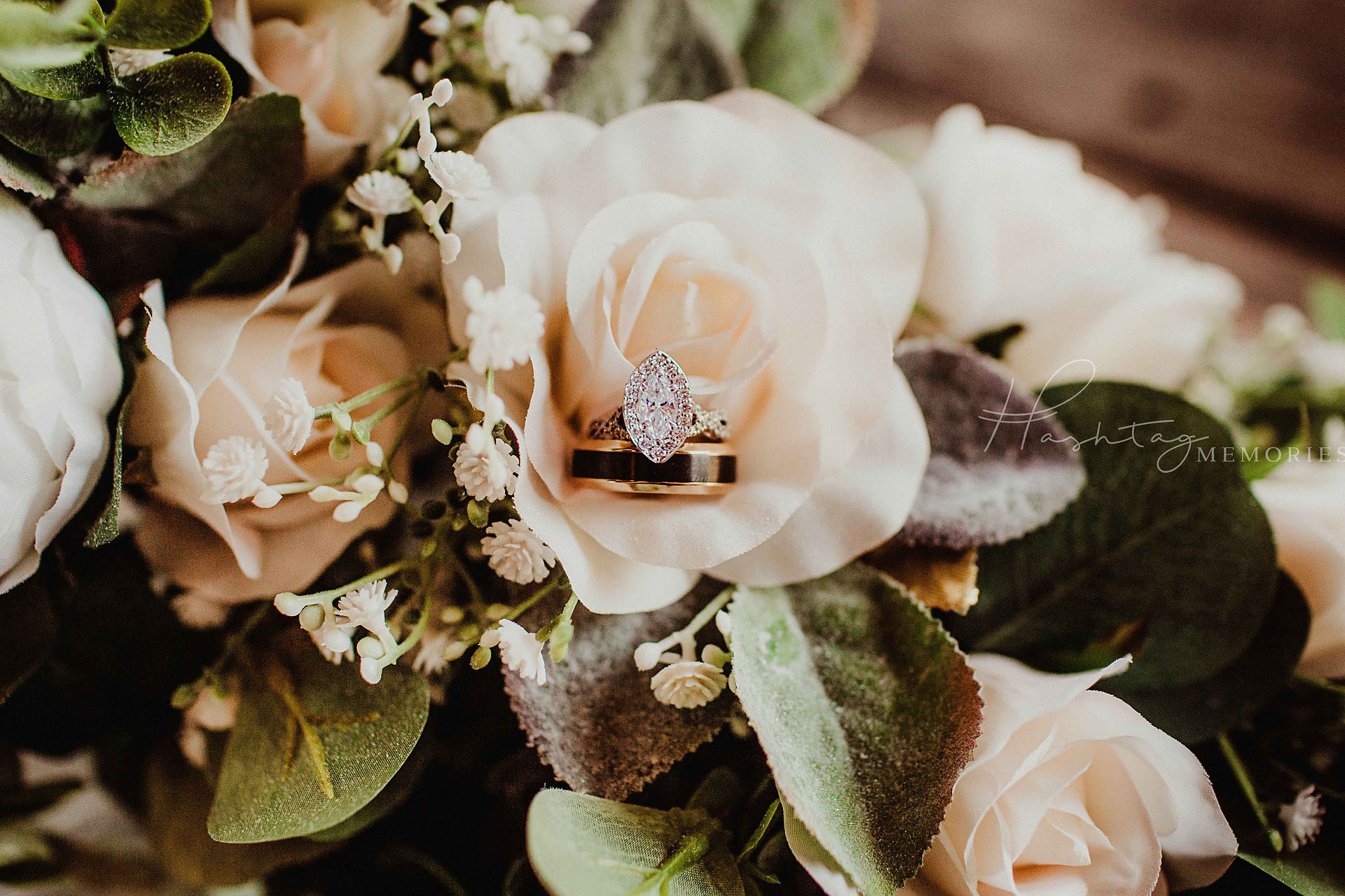 bride's marquise engagment ring sits ontop of groom's wedding band within a white rose on their wedding day