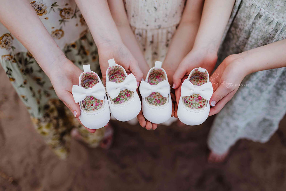 Hands hold four tiny white baby shoes with bows and floral linings, surrounded by floral dresses; Memories watermark.
