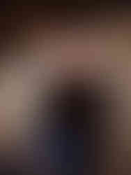 groom to be in mid 20s looks at camera for portrait during engagement session. he's wearing jeans, a black long sleeve shirt and a black truckers hat that is embordered with the couples 2022 summer wedding date