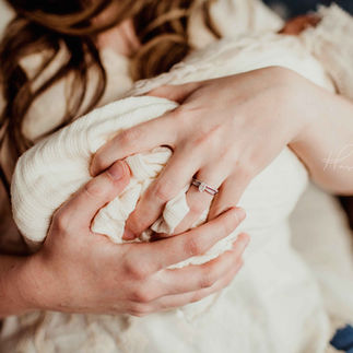 newborn baby girl held in cream colored blanket and baby bonnet, in her mother's arms during baby's newborn photo shoot in central indiana