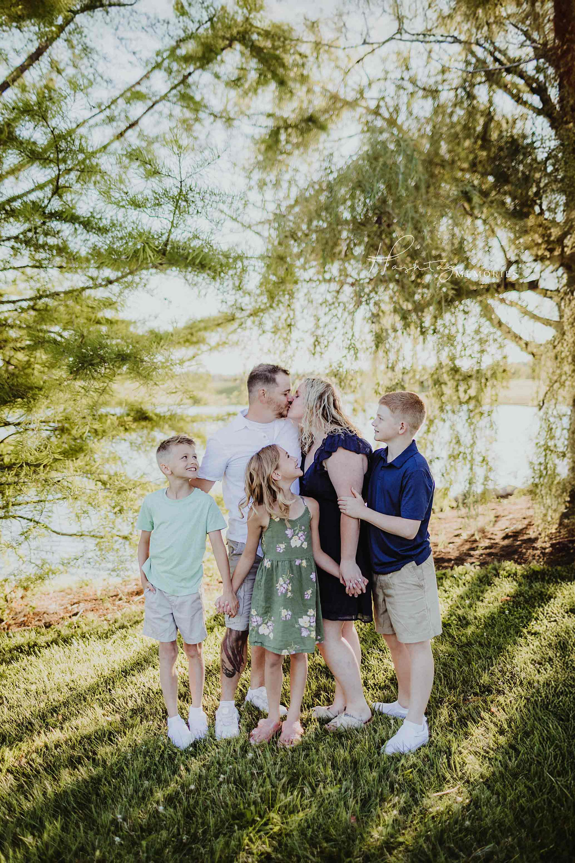 family stands infront of willows and trees at coxhall gardens on a lake during family photo shoot with Hashtag Memories Photography