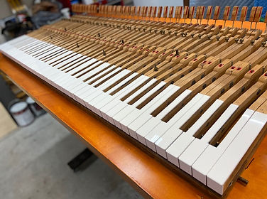 Piano keybed with a freshly installed set of clean white keytops following custom keytop replacement