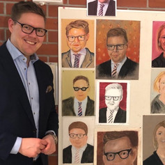 Kansanedustaja Antti Lindtman seisoo seinällä olevien muotokuviensa vierellä.jpeg