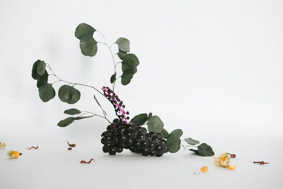 a bunch of black grapes with green leaves on a white surface