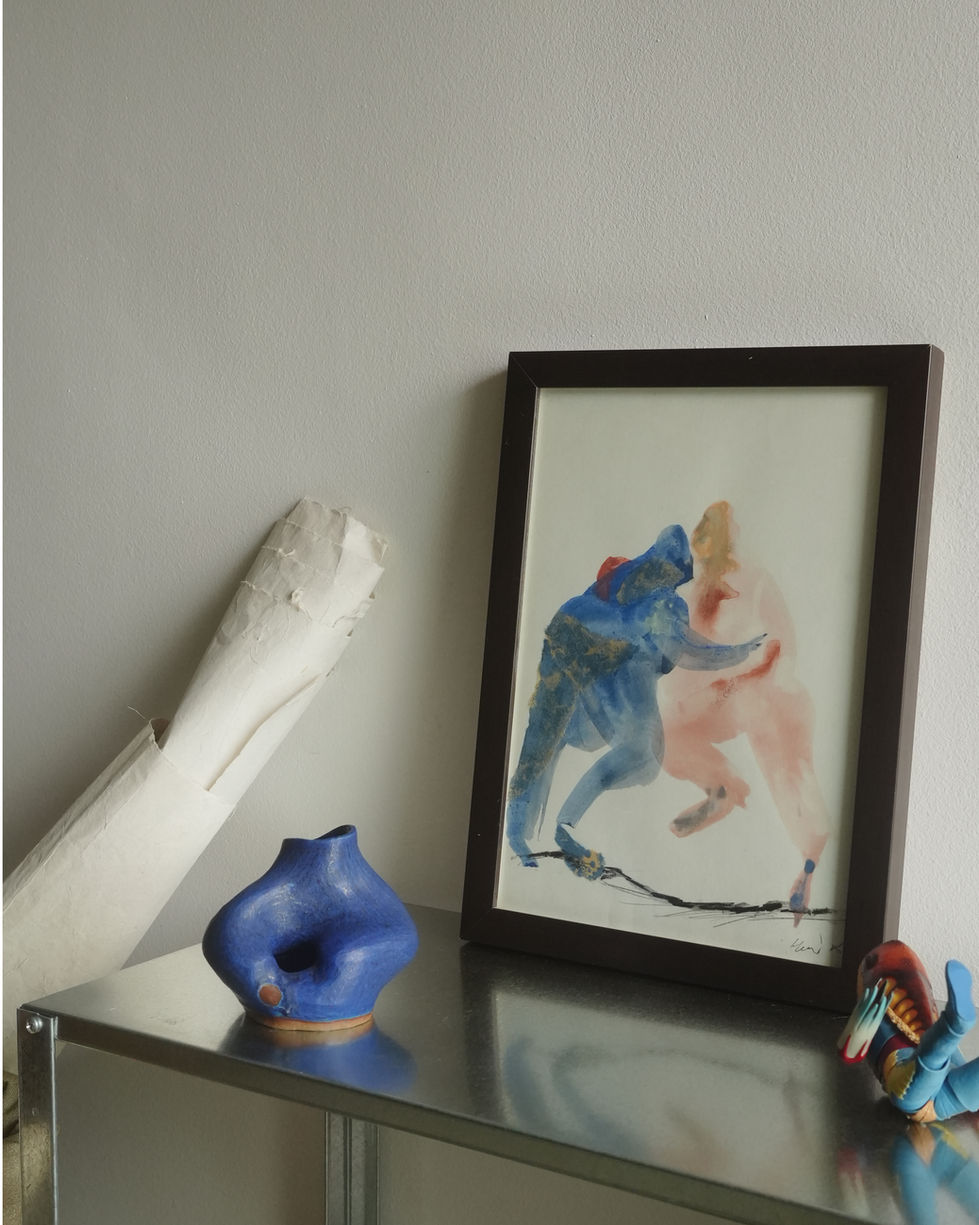 a framed painting of two people is on a table next to a blue vase