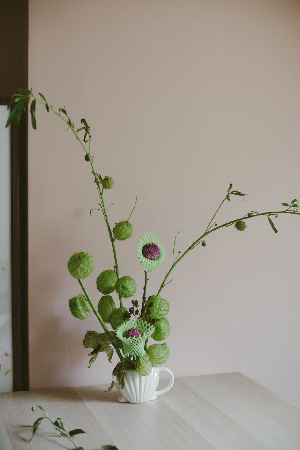 a vase filled with green and purple flowers against a pink wall