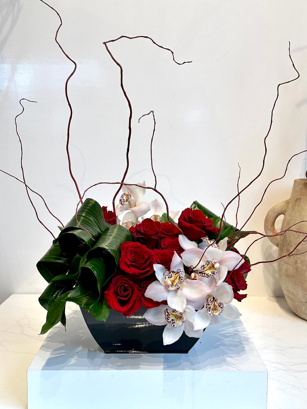 Roses and orchids with leaves in a black vase