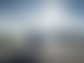 Ein Mann steht auf einem Flugfeld bei Sonnenschein neben einem weißen Hubschrauber, vor einem großen Hangar.