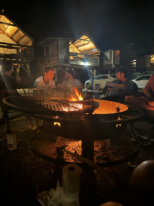Various members of the group sit in front of a bonfire, enjoying the warmth.
