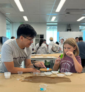 Jeff smiles and points at the various weighboats containing solutions of calcium chloride and sodium alginate for the young girl visiting.