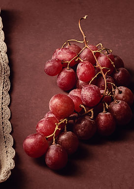 Racimo de uvas rojas sobre fondo burdeos acompañado por una tela de lino
