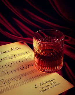 Vaso bajo con bebida ámbar sobre una partitura en una escena editorial de luz cálida.