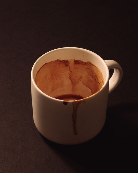 Fotografía editorial de taza blanca con restos de café en el borde, minimalismo oscuro, estilo autoral.