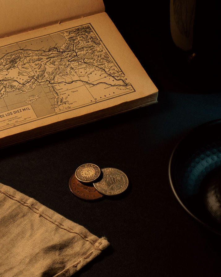 Fotografía editorial de mapa antiguo con monedas y papeles sobre mesa oscura, estilo narrativo y sofisticado.