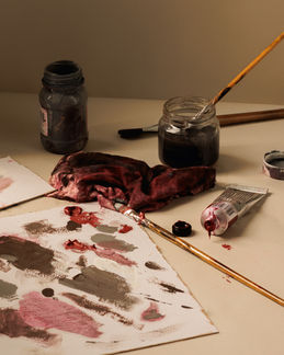 Pinceles, frascos de pigmento y manchas de pintura sobre una mesa de trabajo en una composición editorial cálida.