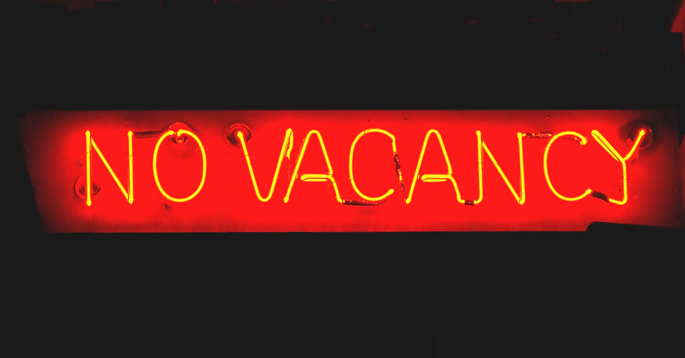 Neon sign displaying "NO VACANCY" in bright yellow against a red background, evoking a sense of unavailability or full capacity.