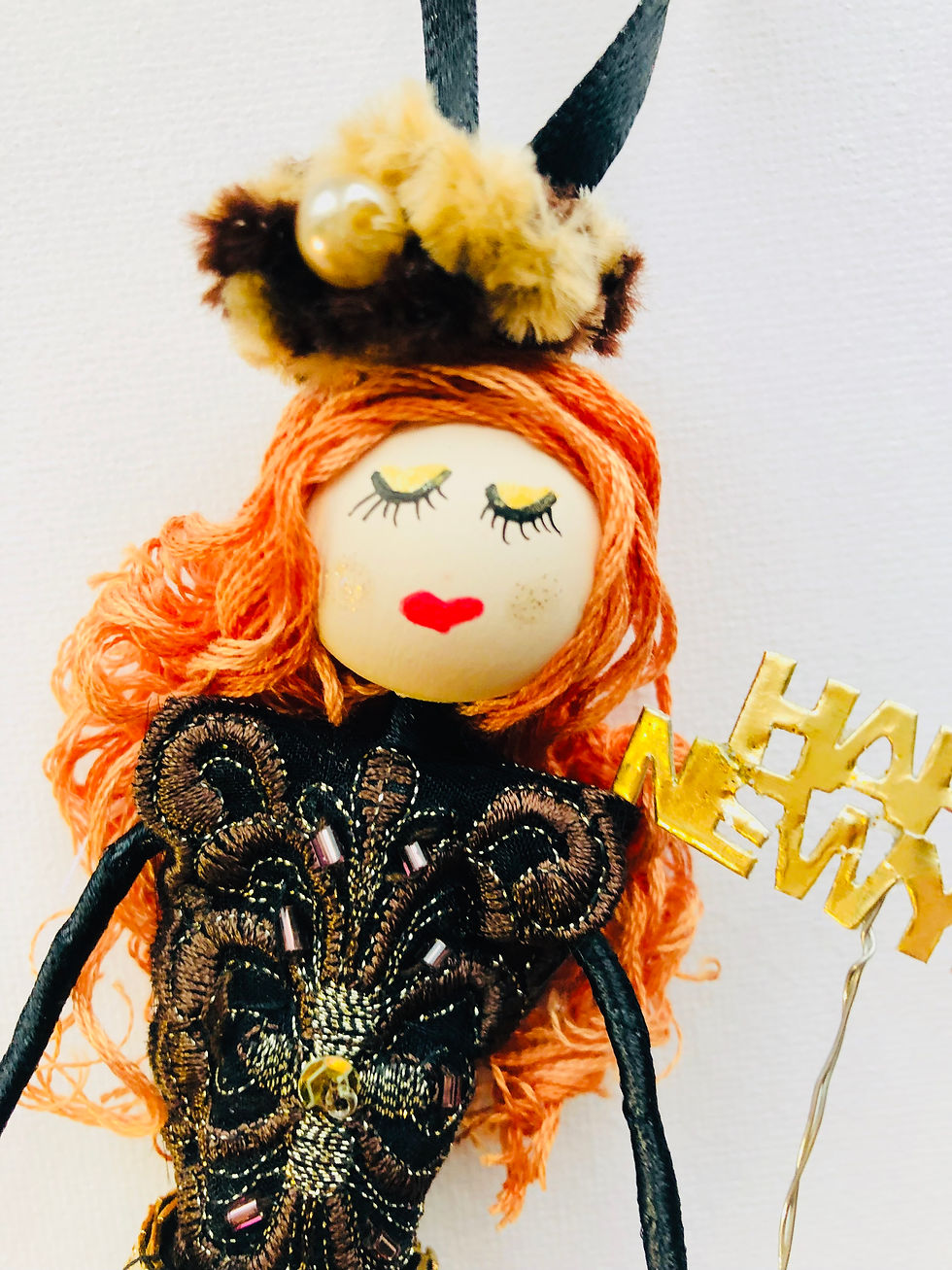 Thumbnail: red headed doll with leopard hat and skirt holding Happy New Year sign