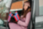 A woman with warm clothes and Norwegian flags in her hands looks straight ahead as she stands inside a car with the door open.