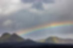 A cloudy sky with a beautiful rainbow crossing it stretches across the mountains of the Icelandic Highlands.