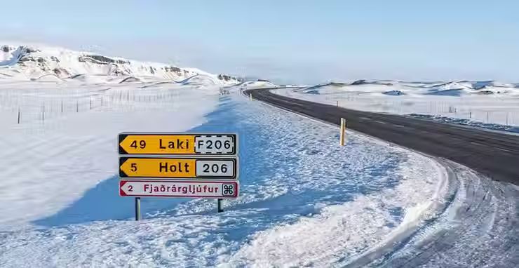 Vista general de una carretera de asfalto islandesa en invierno, completamente cubierta de nieve, donde una señal de tráfico amarilla destaca entre las blancas e indica la proximidad de carreteras F.