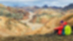 A woman in hiking gear poses with Iceland's colorful Landmannalaugar National Park behind her.