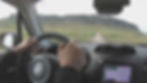 Hands grip the steering wheel of a Jeep as it navigates along a dirt road in Iceland.