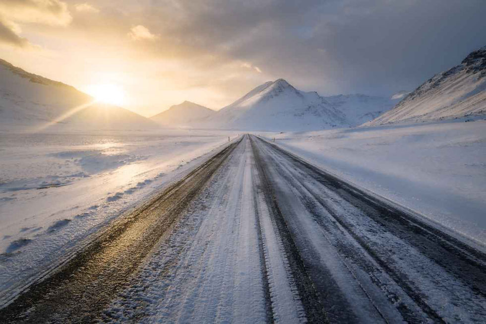Carretera parcialmente helada entre montañas nevadas al amanecer, con luz baja y firme resbaladizo típico del invierno islandés.