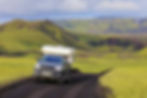 A black 4x4 vehicle with a white tent drives along an unpaved road surrounded by vegetation in the Icelandic Highlands.