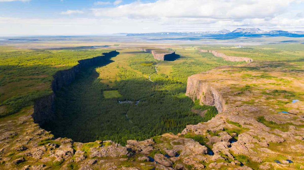 Drone view of the Ásbyrgi canyon in Iceland with vegetation at its peak and blue sky.