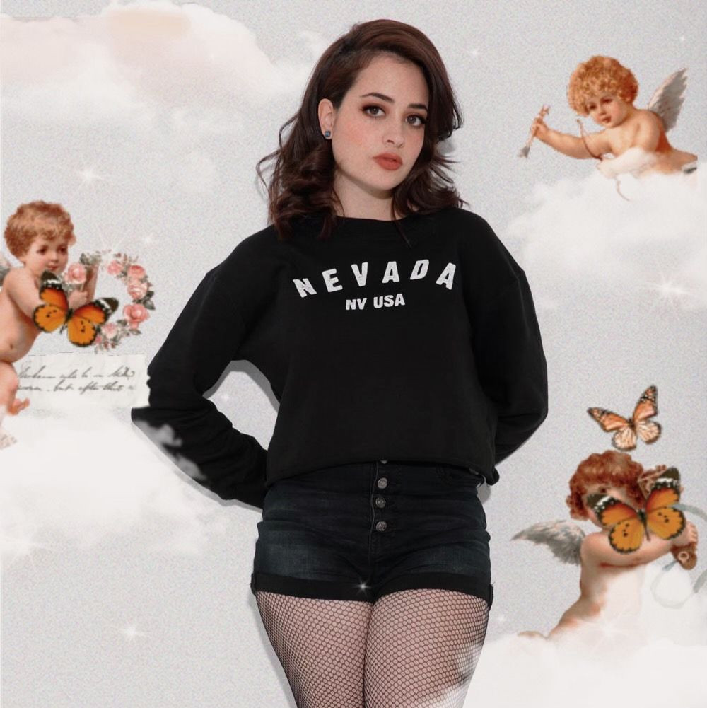 Singer Karamilk standing in front of a backdrop of cherubs, clouds and butterfiles