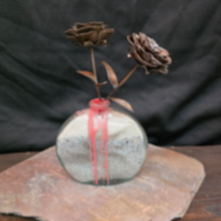 Handmade metal flower sculpture with layered steel petals arranged in a glass vessel
