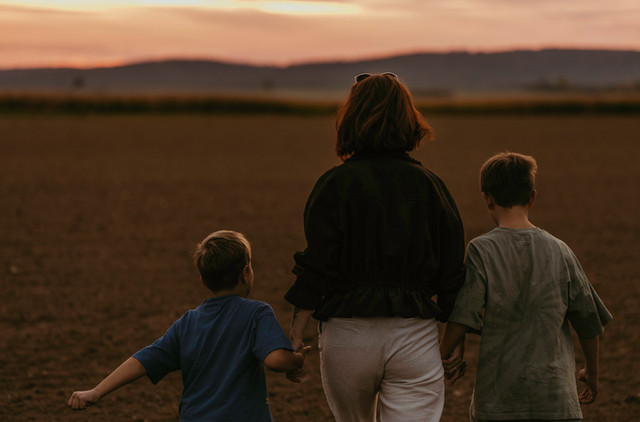 Lena mit ihren beiden Söhnen, von hinten, Hand in Hand auf einem Feld im Abendlicht