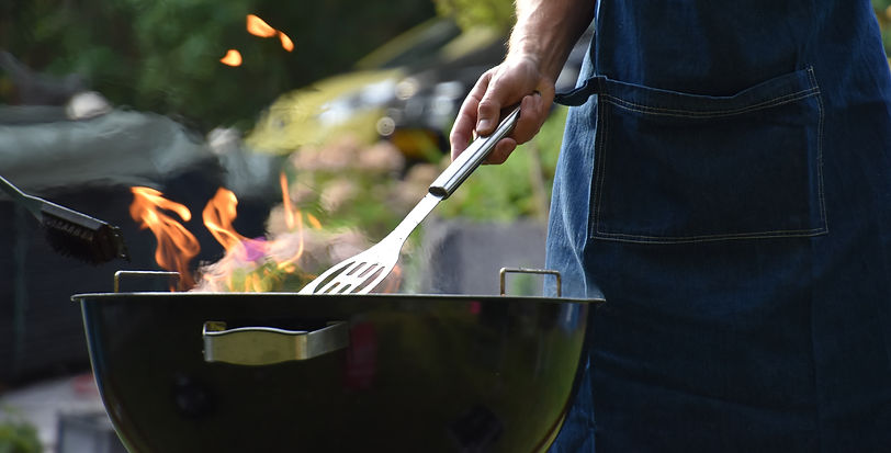 Person in blue apron using a spatula on a flaming grill