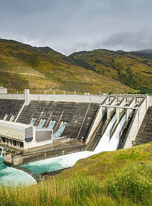 Wasserkraftwerk mit fließendem Wasser, Berge im Hintergrund, grüne Wiesen, IMB, Naturlandschaft.