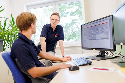 Zwei Mitarbeiter diskutieren vor Computer mit Daten im Büro, E.GRUPPE.
