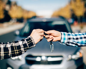 Two people doing a fist bump in front of a blue rental car in a scenic outdoor location