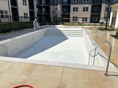 A rectangle apartment complex pool that has white plaster, an ADA chair, and a fence surrounding the area.
