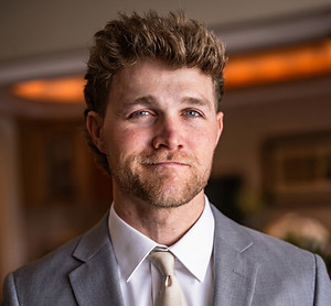 Bryce Herrema, with curly hair in a grey suit and tie.