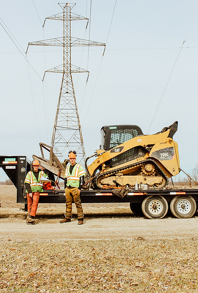 Two workers with a yellow skid steer on a trailer.