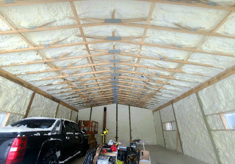 Garage interior, wooden rafters, white spray foam insulation, and black truck.