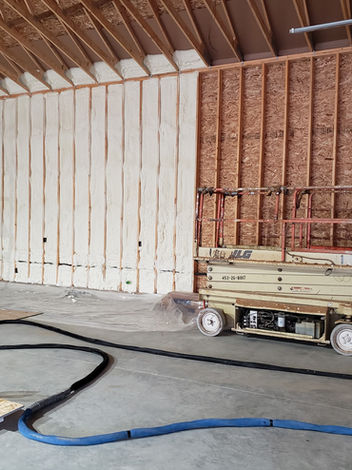 Spray foam insulation applied to wall in large unfinished construction room.