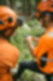 Two workers in orange safety gear looking at a device outdoors.